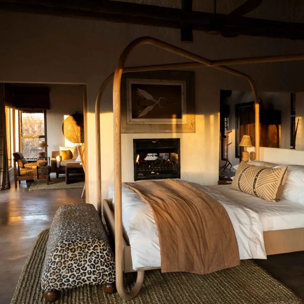 Wooden canopy bed with patterned bench in a cozy rustic room with fireplace
