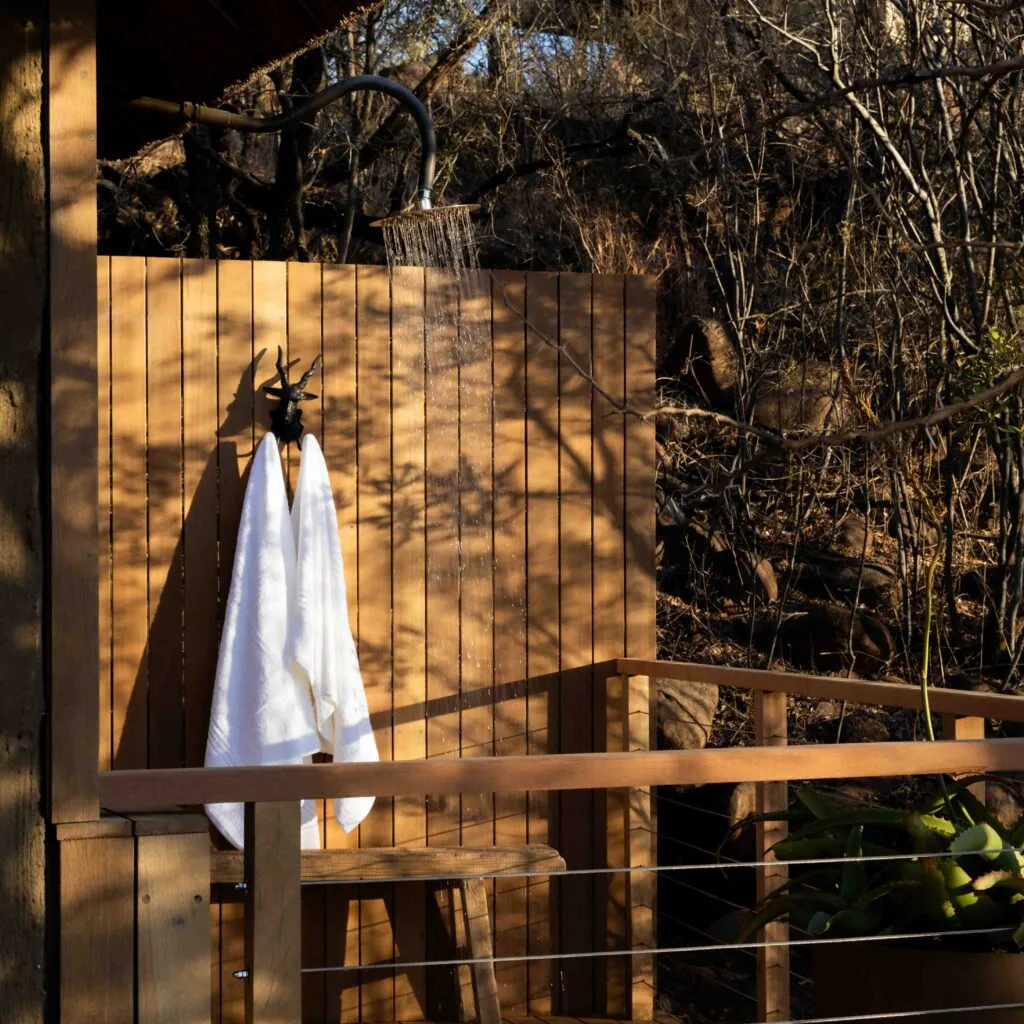 Outdoor wooden shower with towel hanging surrounded by trees
