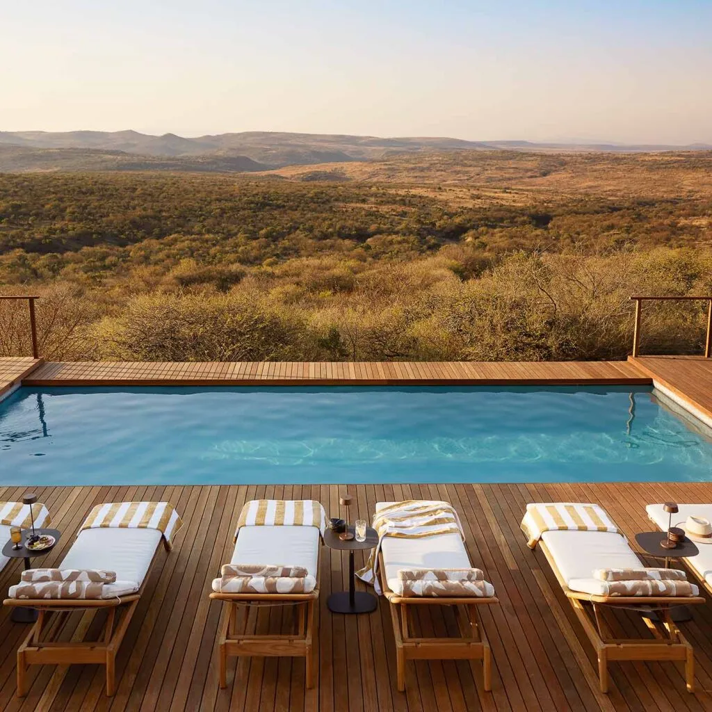 Three lounge chairs by a pool with a scenic landscape view
