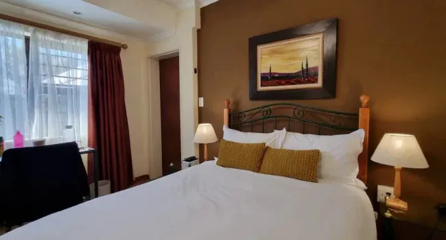 Bedroom with a bed two lamps a desk and a landscape painting on the wall