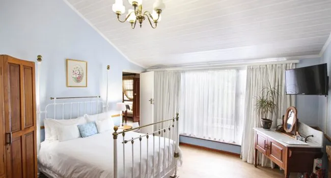 Bright bedroom with white iron bed wooden wardrobe and large window with curtains