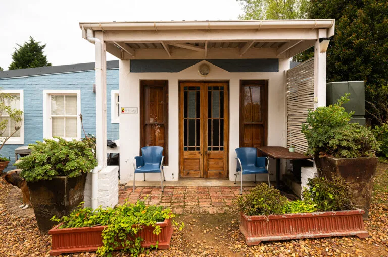 Small house with wooden door blue chairs and potted plants on brick patio