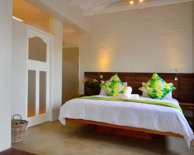 Bright bedroom with white bed green pillows and wooden headboard against white brick wall