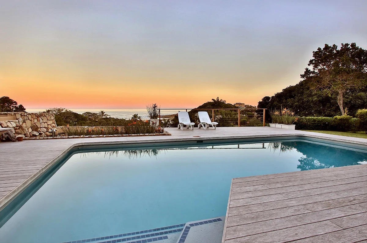 Swimming pool with deck and lounge chairs overlooking sunset and ocean view