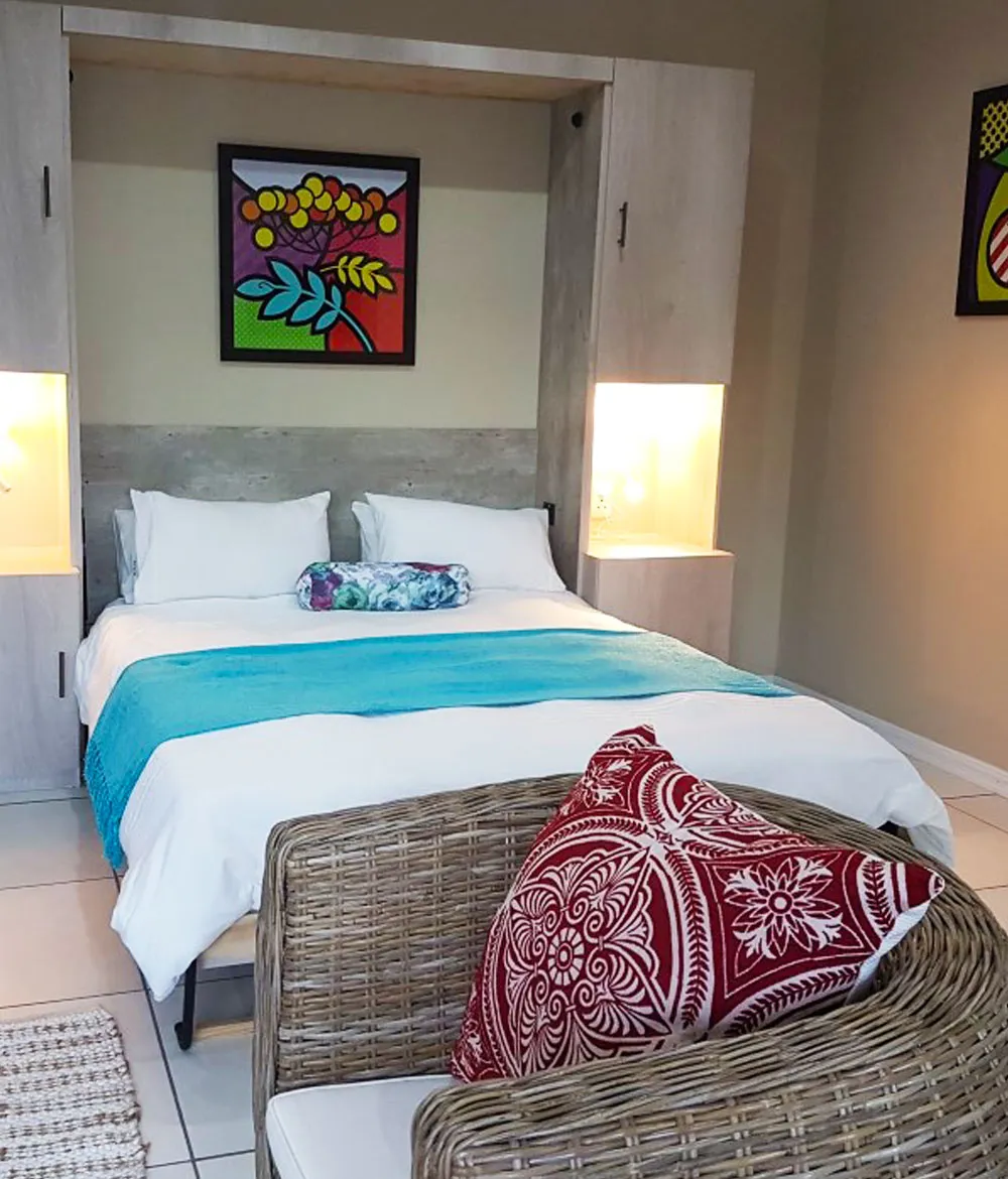 Bedroom with a bed colorful pillows and a wicker chair in front