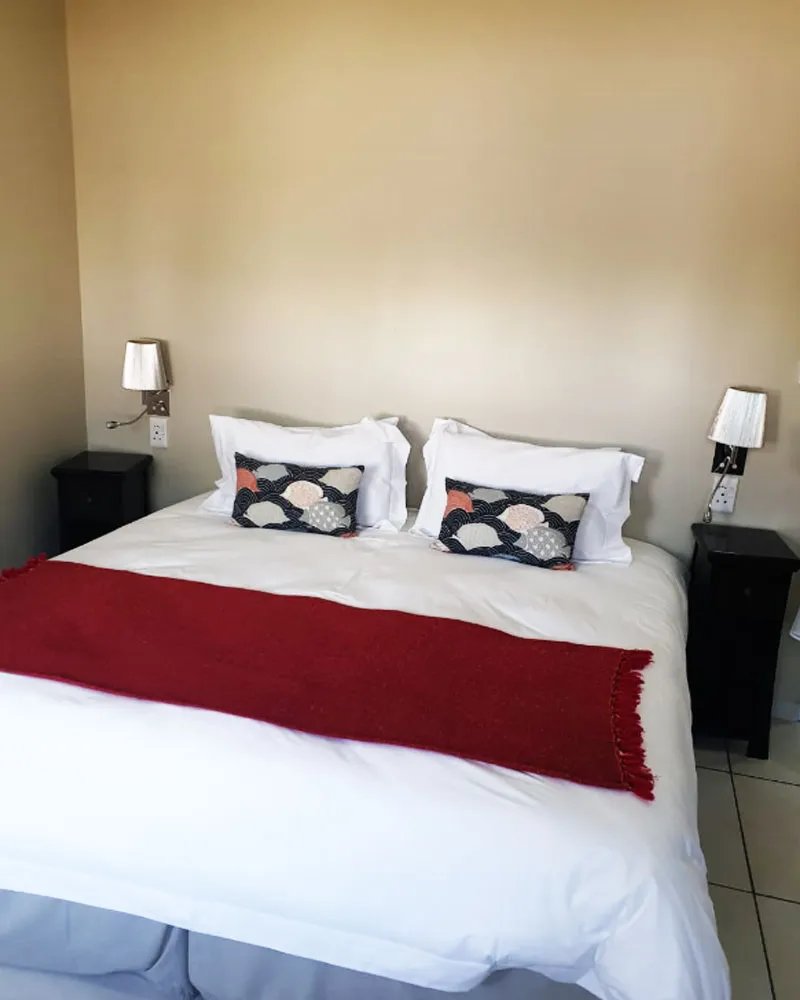 A neatly made bed with red throw and patterned pillows in a bedroom