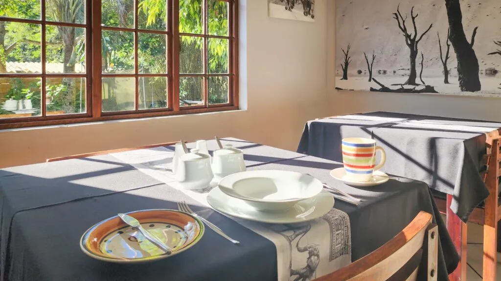 Dining table set with plates cutlery and mugs near a window with a view