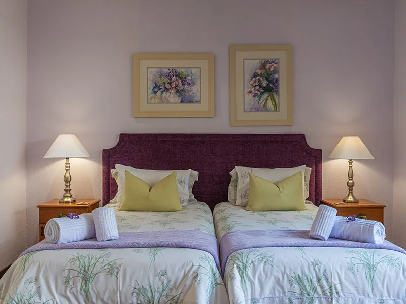 Two twin beds with floral bedding in a purplewalled bedroom with floral artwork