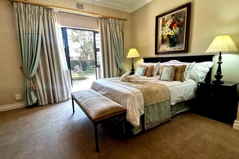 Cozy bedroom with large bed open curtains and garden view through glass doors