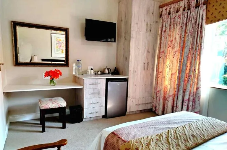 Cozy bedroom with a bed desk TV and floral curtains