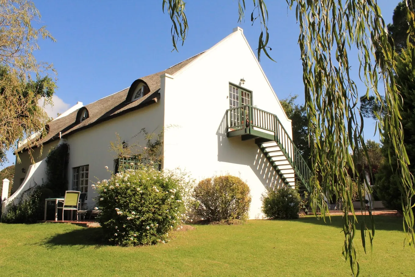 White house with green staircase and surrounding greenery under blue sky