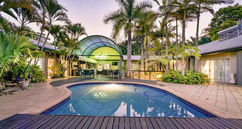 Tropical backyard with pool palm trees and modern house at dusk