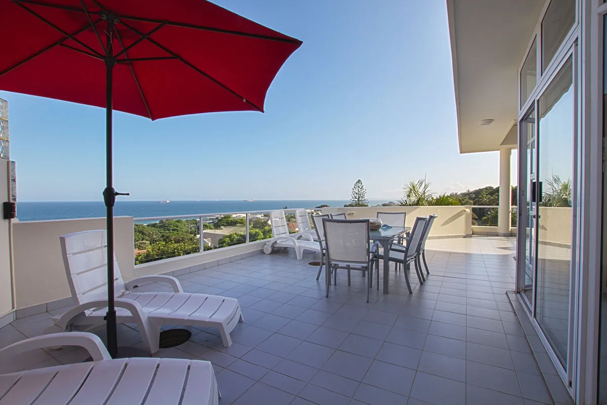 Patio with lounge chairs dining table and ocean view under a red umbrella