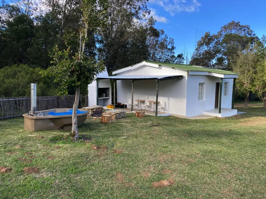 Small white house with a veranda in a grassy yard with trees