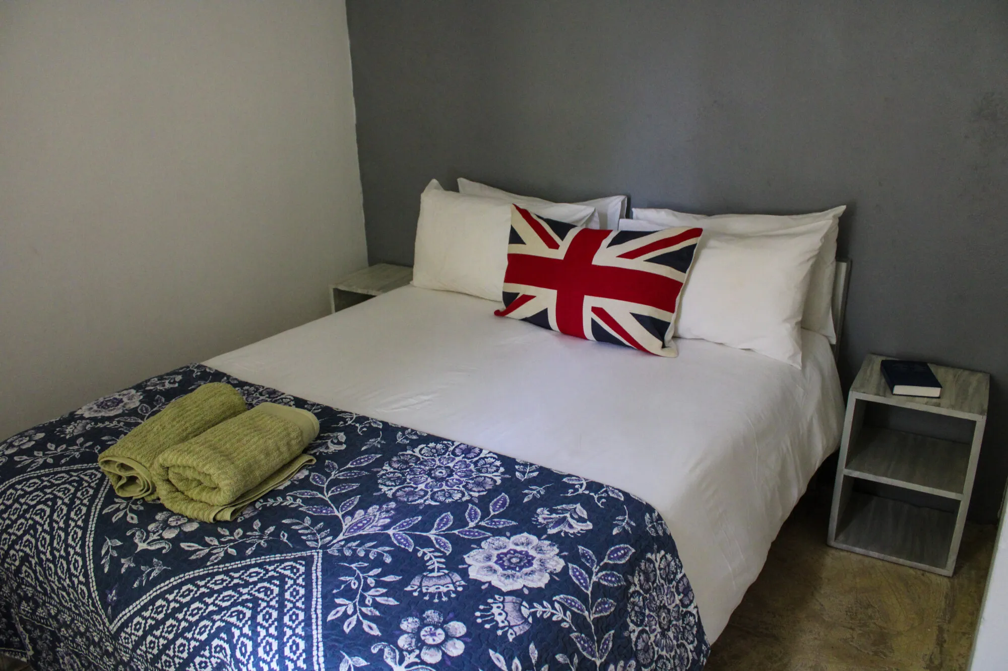 A bed with a Union Jack pillow green towels and floral blanket in a bedroom