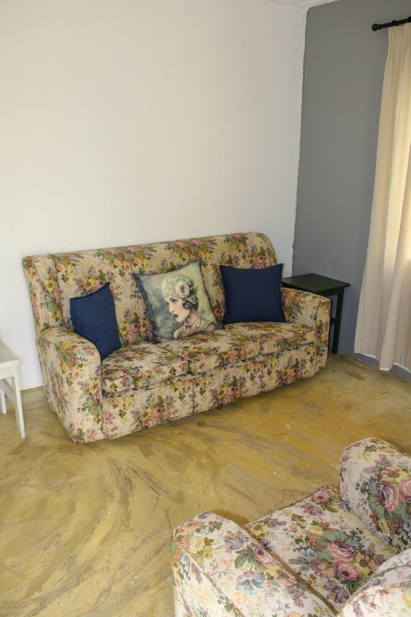 Floralpatterned sofa and armchair in a room with wooden floor and curtains