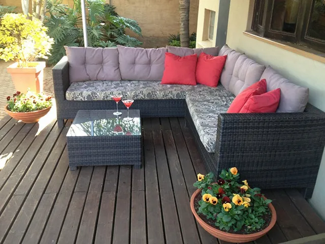 Outdoor patio with wicker sofa glass table and potted flowers on wooden deck