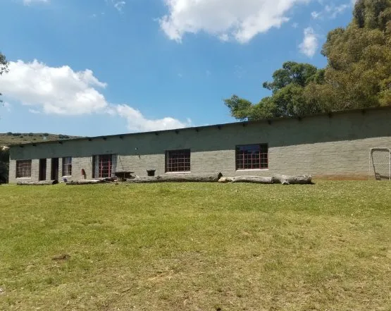 Long singlestory building with windows grassy field trees and blue sky