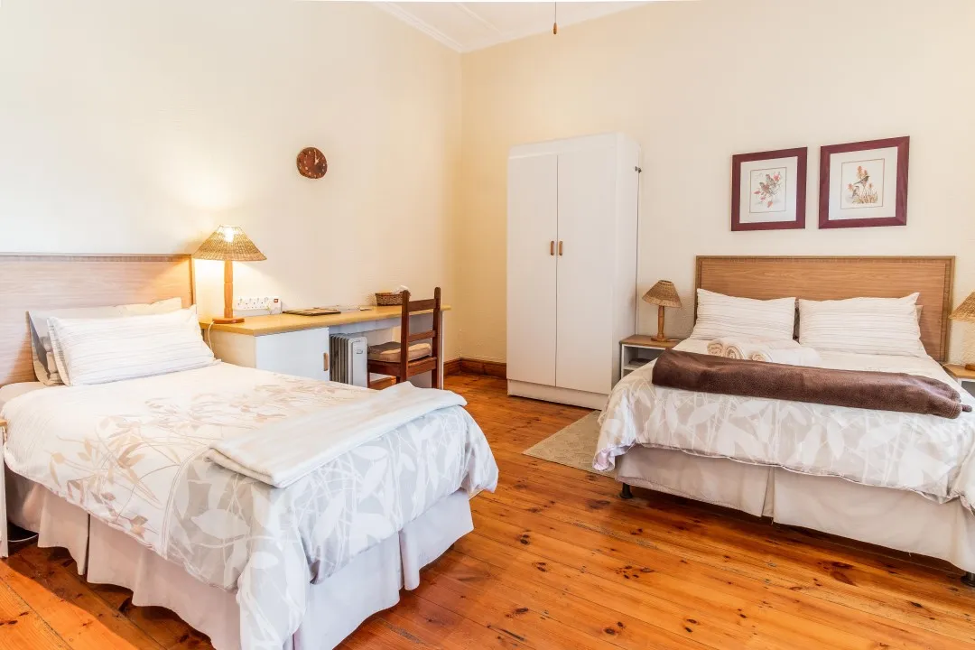 Two beds in a tidy welllit bedroom with wooden flooring and furniture