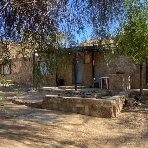 Stone house with outdoor seating area under trees in sunny weather