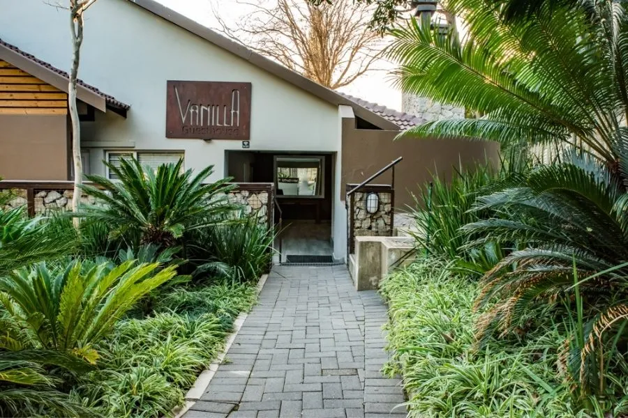 Pathway leading to a building entrance with lush greenery and a sign VinillaH