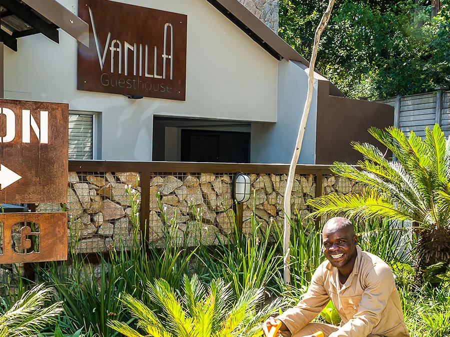 Man gardening in front of a guesthouse sign with lush greenery around
