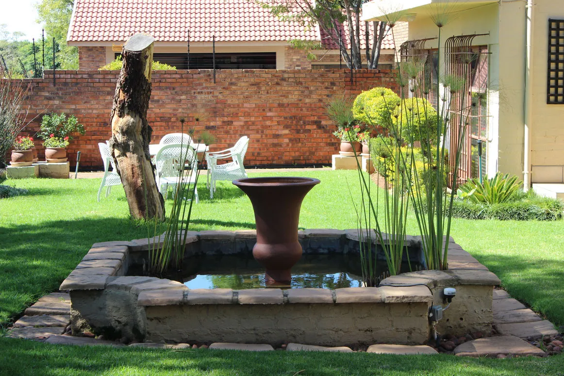 Small water fountain in a garden with green grass and brick wall background
