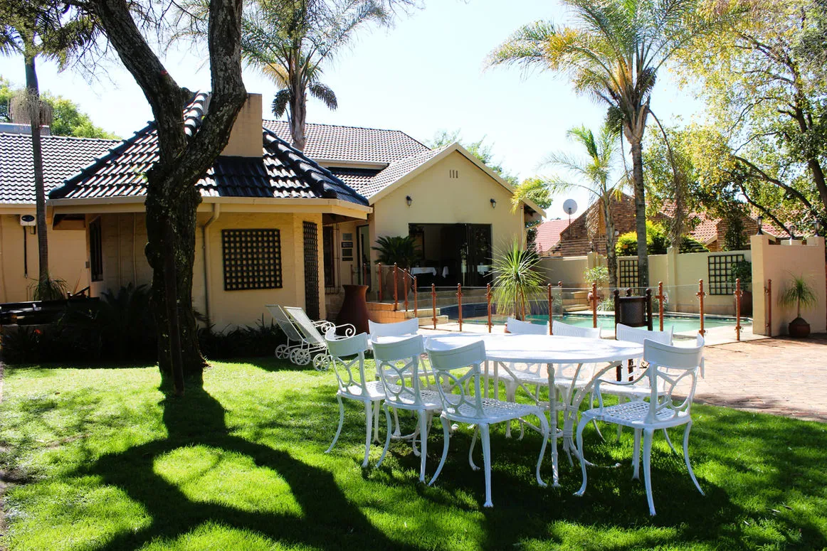 Garden with white patio furniture trees and a house in the background