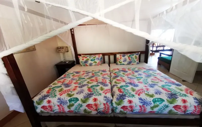 Bedroom with two single beds under a mosquito net floral bedding and bedside table