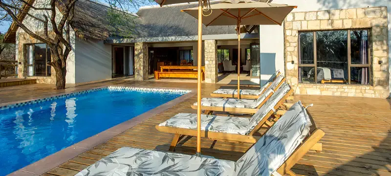 Swimming pool with lounge chairs on a wooden deck beside a house