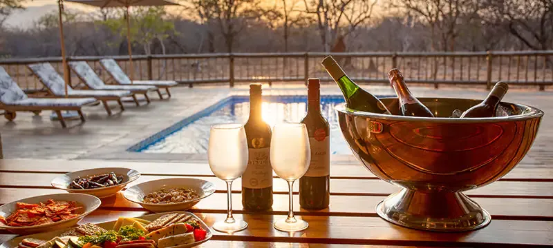 Outdoor dining setup with wine glasses and food by a pool at sunset