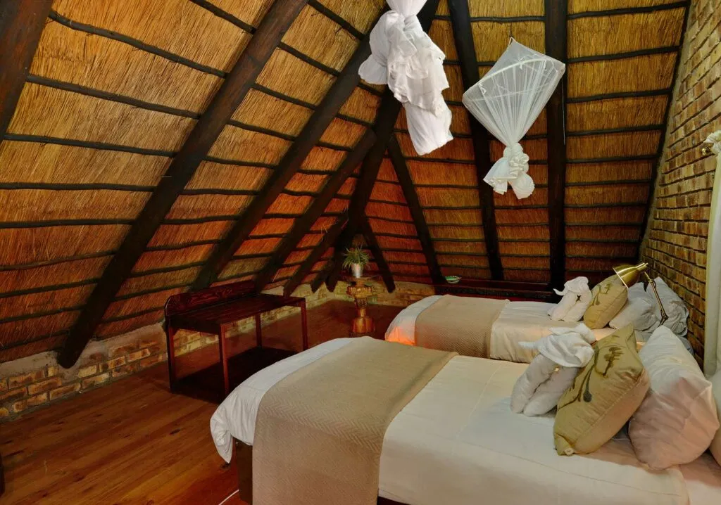 Cozy bedroom with two beds thatched ceiling and mosquito nets