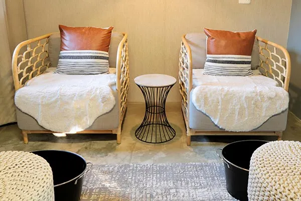 Two cozy chairs with pillows and throws a small table and poufs in a lounge