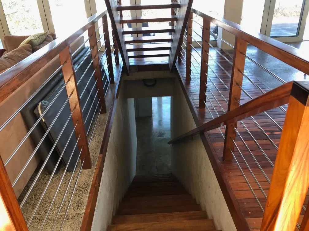 Wooden staircase leading to a lower level with glass railings and natural light