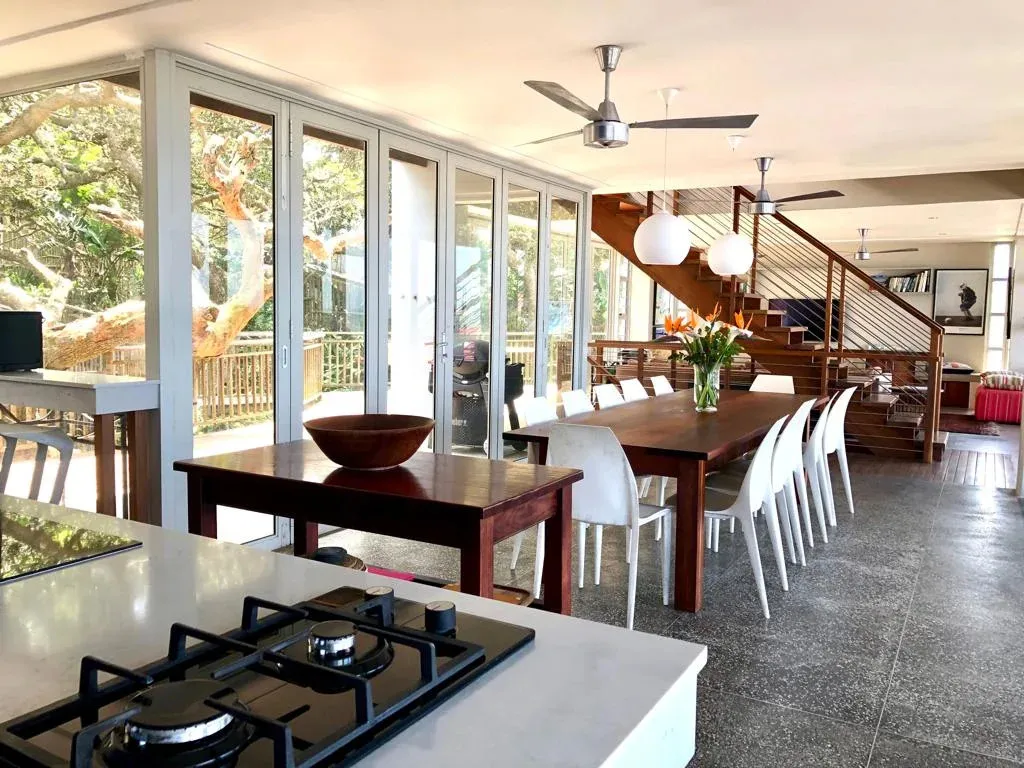 Modern kitchen and dining area with large windows and staircase in background