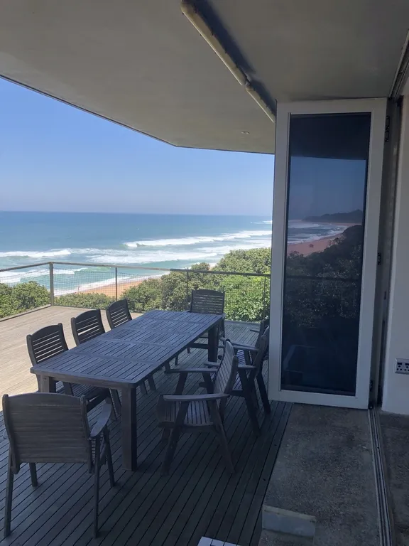 Wooden table and chairs on a deck with ocean view and greenery