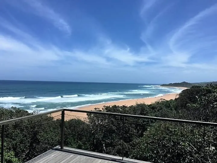 Ocean view from a deck with sandy beach and greenery in the foreground