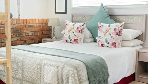 Cozy bedroom with a neatly made bed floral pillows and brick wall