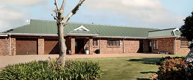 Singlestory brick house with green roof and large front yard with trees