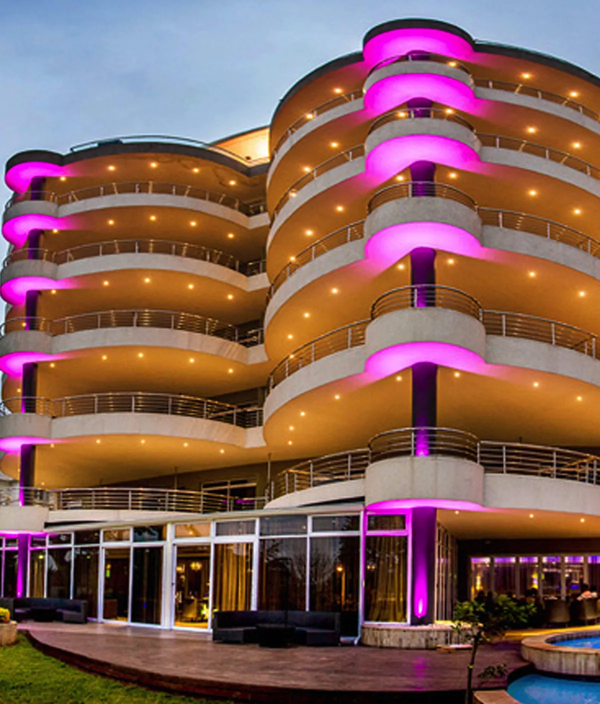 Modern building with curved balconies lit by pink and yellow lights at dusk