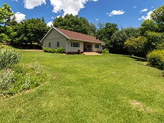 Singlestory house with a red roof in a lush green yard
