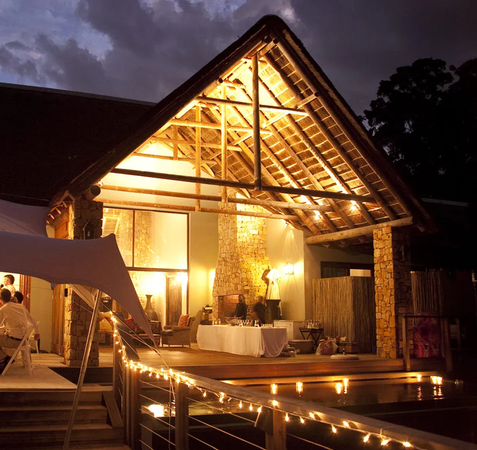 Wooden lodge with lit interior at night people inside outdoor deck