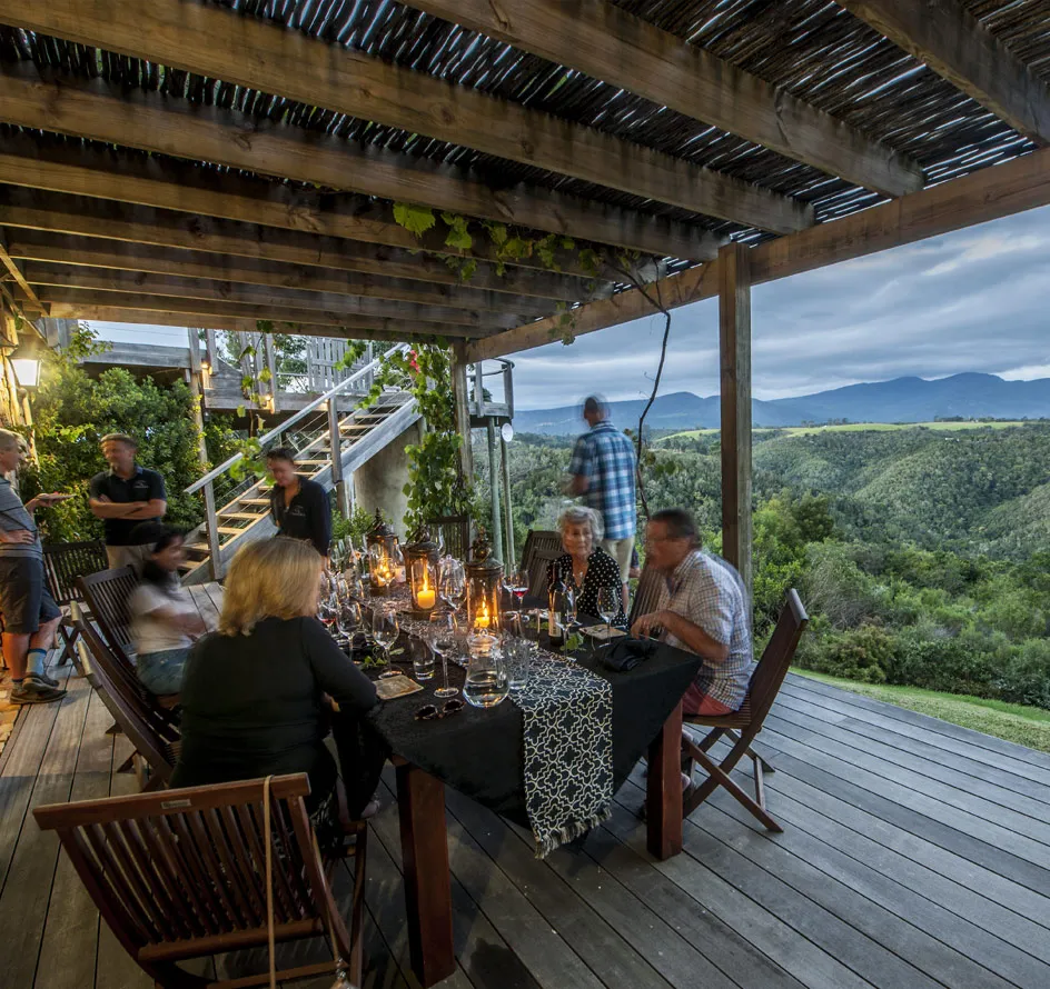 People dining at a wooden table on a deck with scenic mountain views