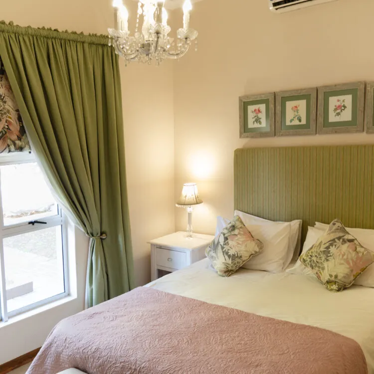 Bedroom with green curtains floral pillows and a chandelier above the bed