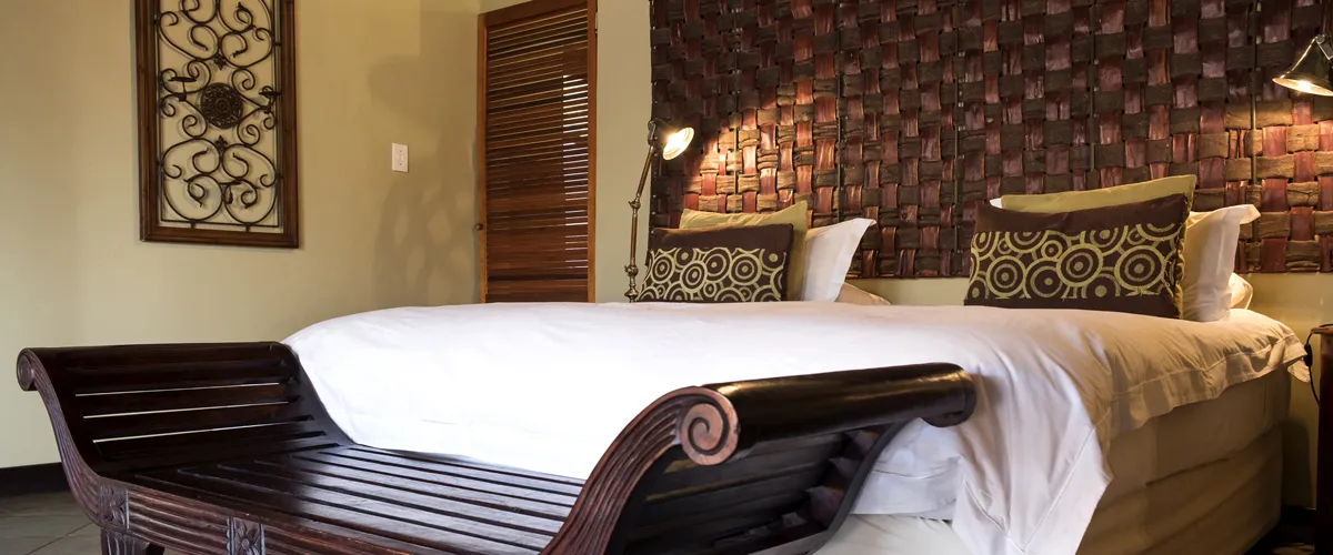 Wooden bench at foot of bed with patterned pillows and textured wall