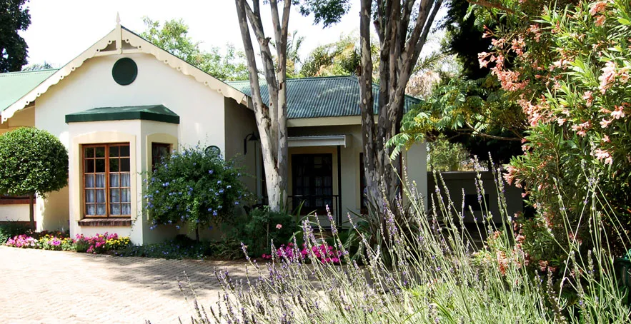 Cottage with green roof and garden surrounded by trees and flowers