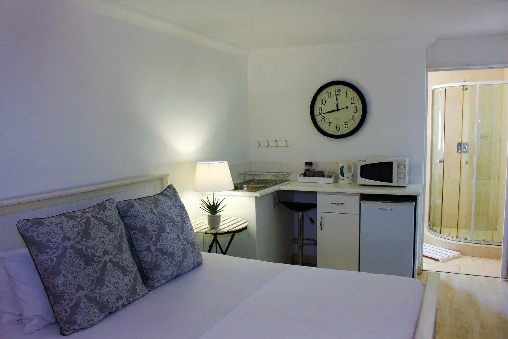 Small studio room with bed kitchenette clock and adjacent shower