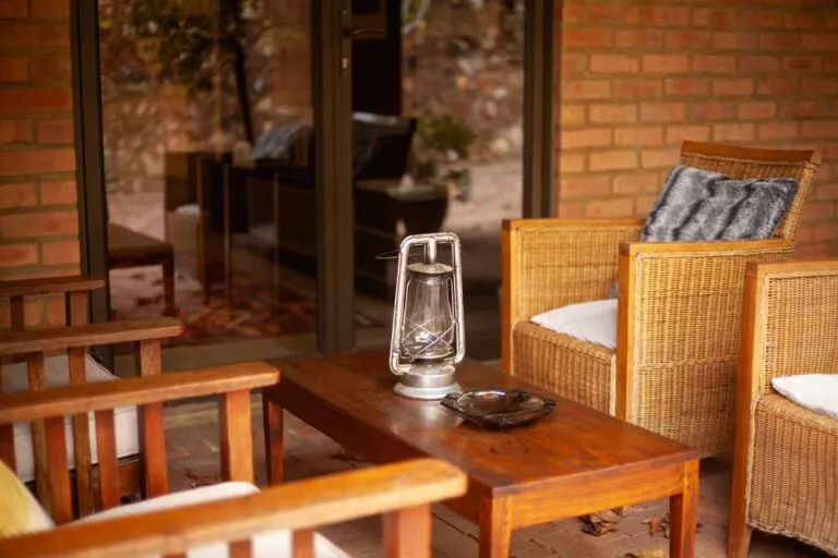 Wooden chairs and table with a lantern on a brick patio near a window