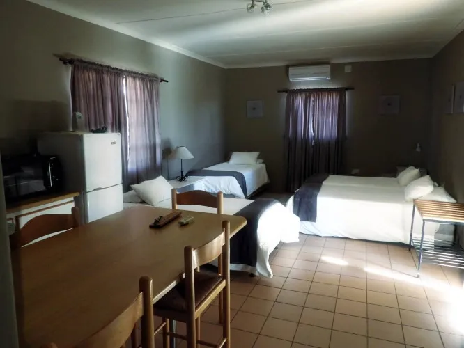 Small bedroom with two single beds a dining table and a refrigerator