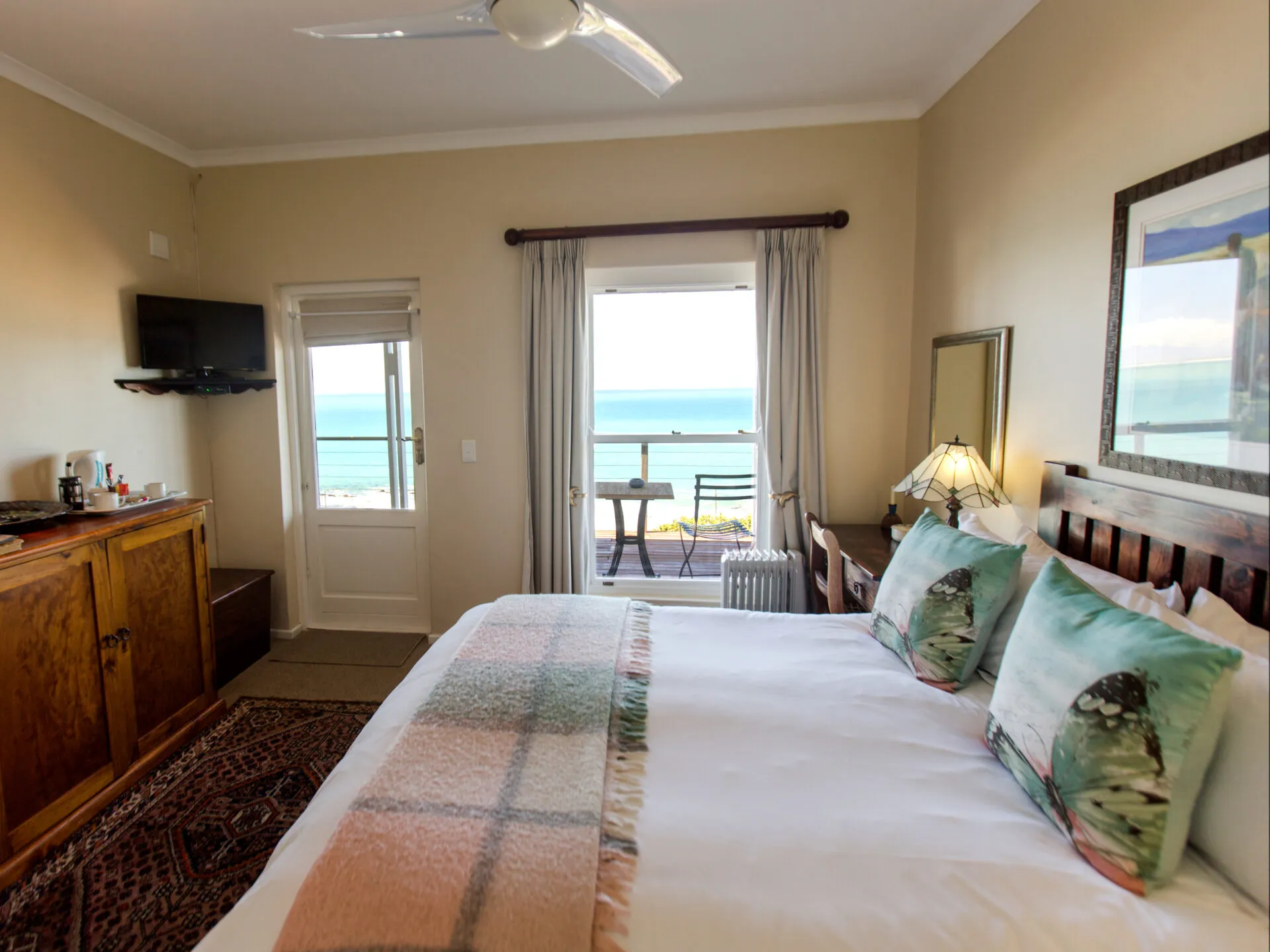 Cozy bedroom with ocean view bed with colorful pillows and wooden furniture